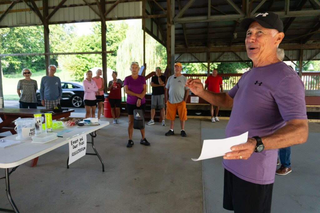 Rick Plunkett, Ellettsville Sports Coordinator, addressing a group at a pickleball event under a pavilion.