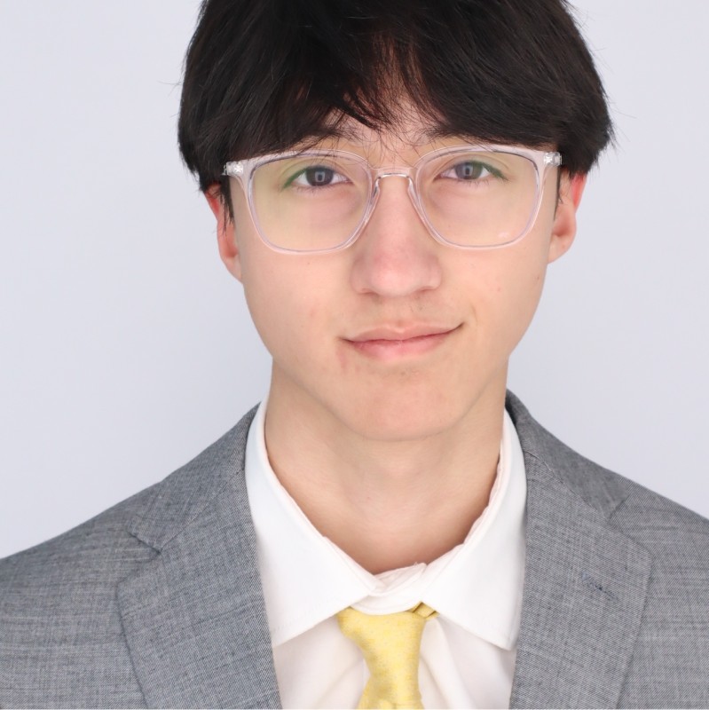 Professional headshot of Ethan Slatkin, a student at Indiana University Bloomington, wearing a light gray suit, white shirt, and yellow tie, with clear-frame glasses and dark hair, against a light background