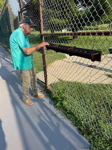 Curt Smith installing a custom wood pickleball paddle rack on a chain-link fence at RCA Park.