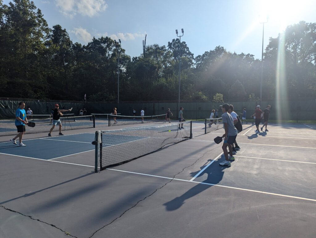 Players engaged in a pickleball game during a ladder event, with sunlight streaming onto the courts at Bloomington Pickleball Club.