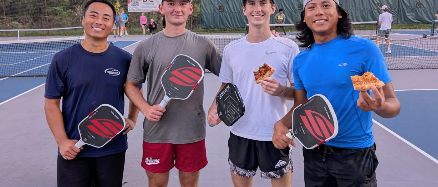 Four smiling pickleball players on court holding Selkirk paddles and pizza slices during a BPC event