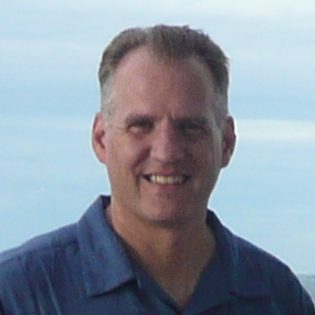Brent Litzer, Bloomington Pickleball Club board member, smiling outdoors with a blue shirt against a serene sky backdrop